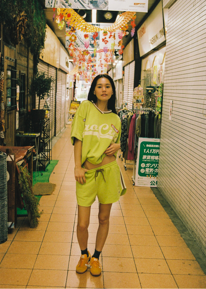 Woman in a bright green lounge jersey and drawstring shorts with CCV branding and logos