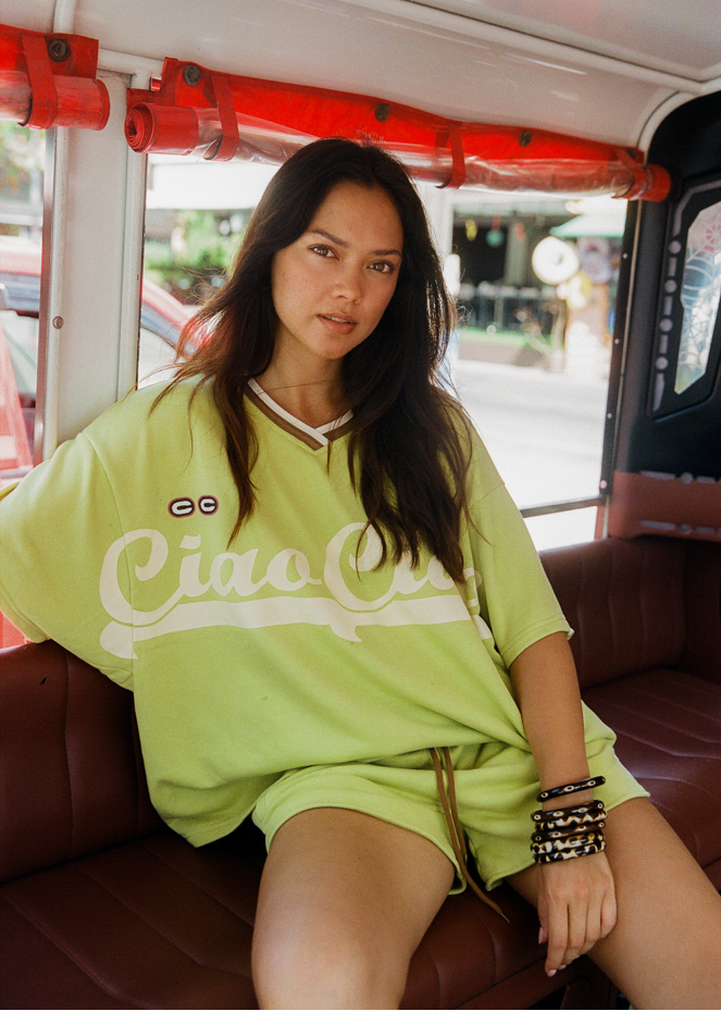 Woman in a bright green lounge jersey and drawstring shorts with CCV branding and logos 