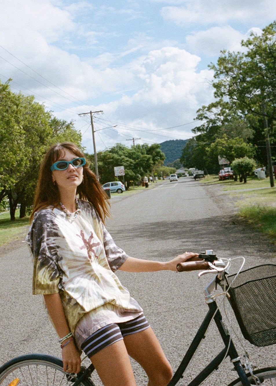 Woman riding a bicycle on a road with tie-dye tee and purple and brown striped bike shorts