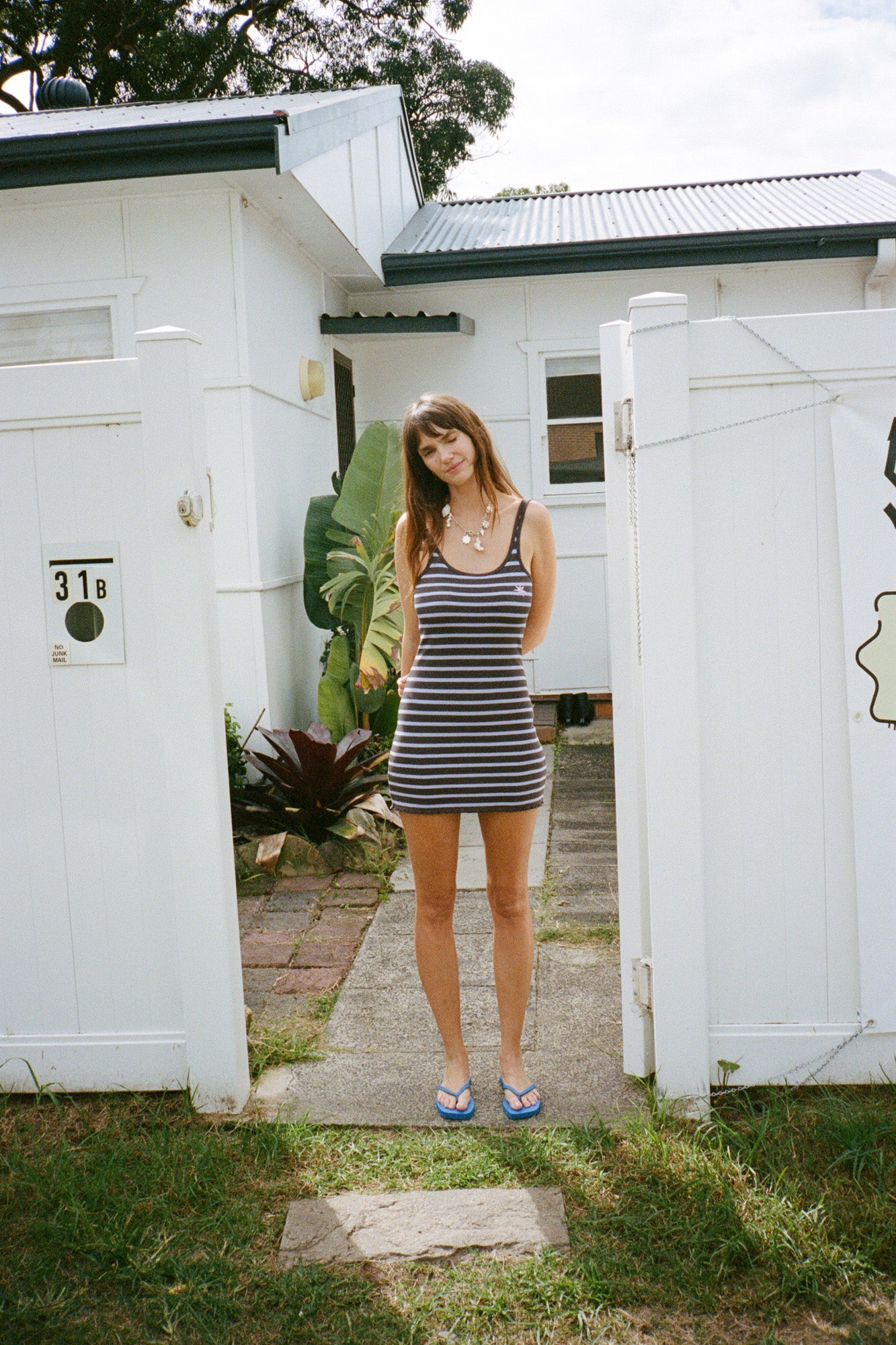 Woman in a purple and brown striped mini dress standing in front of a white house.