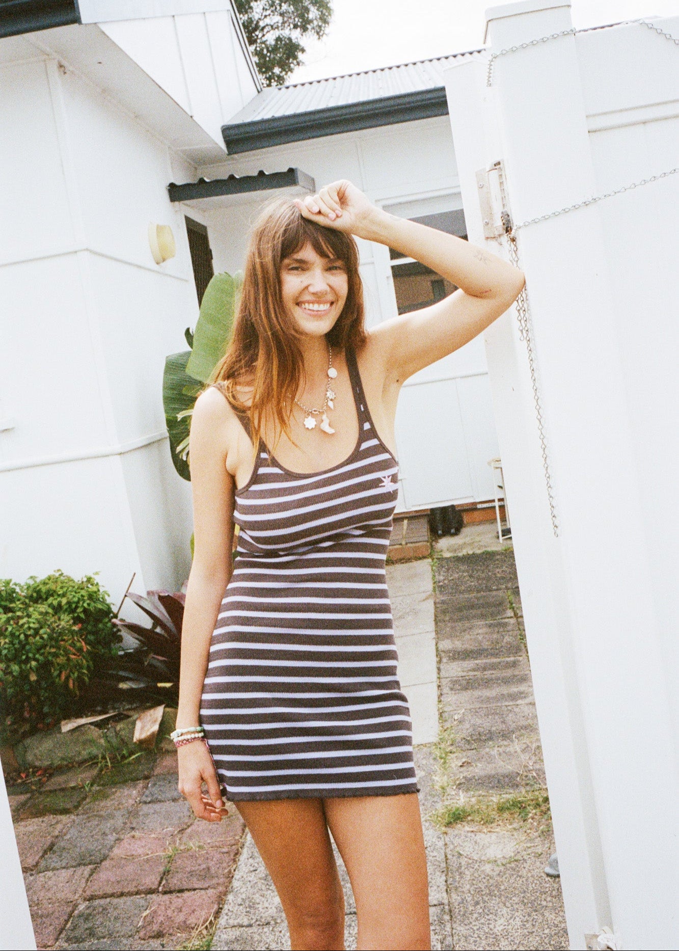 Woman in a purple and brown striped mini dress standing in front of a white house.