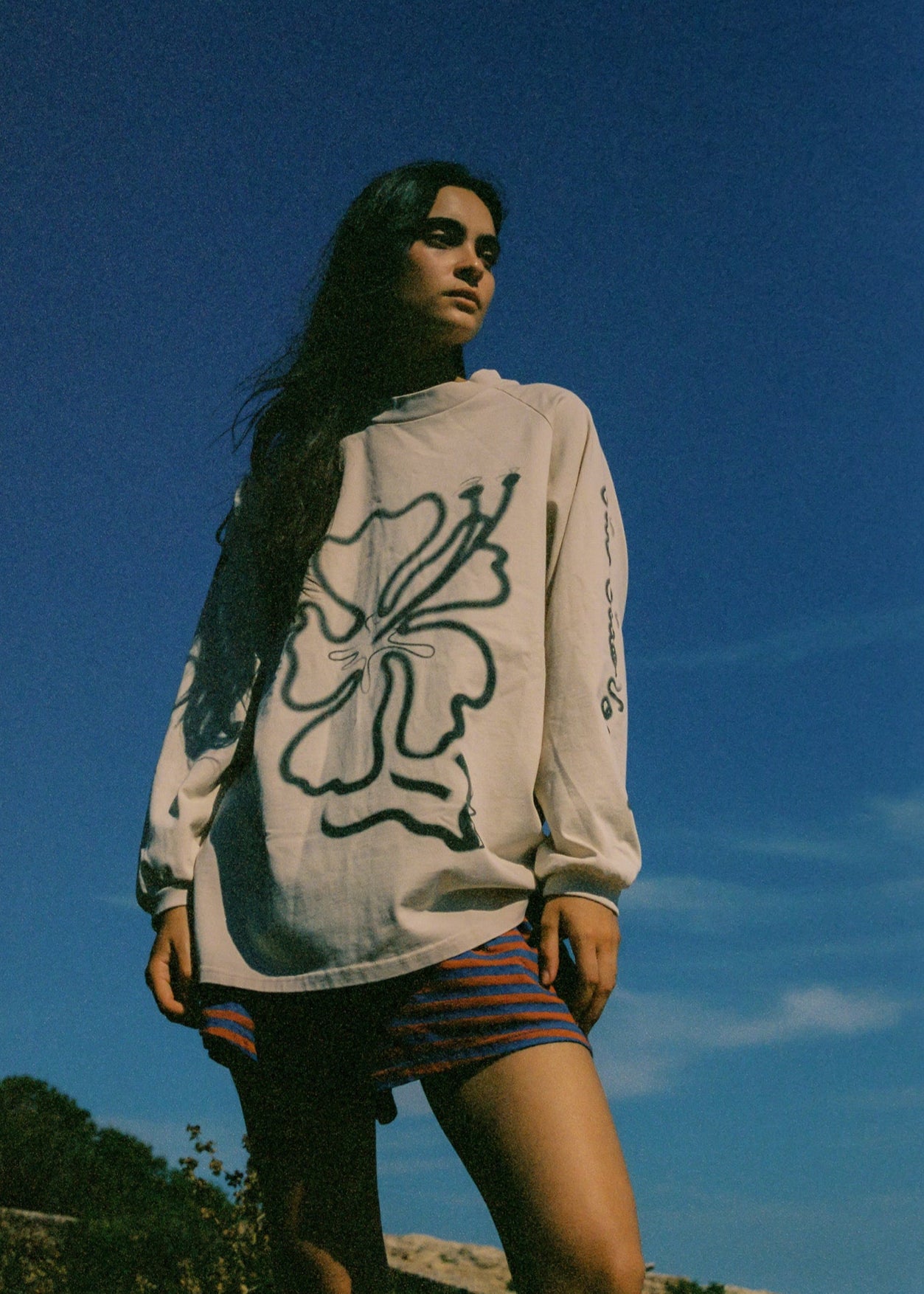 Person wearing a beige oversized long sleeve t-shirt with hibiscus design and a pair of striped shorts.