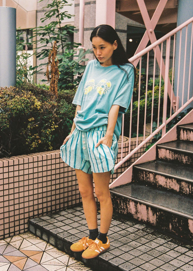 Woman in teal oversized t-shirt with a green crab graphic design and "Ciao Ciao" branding 