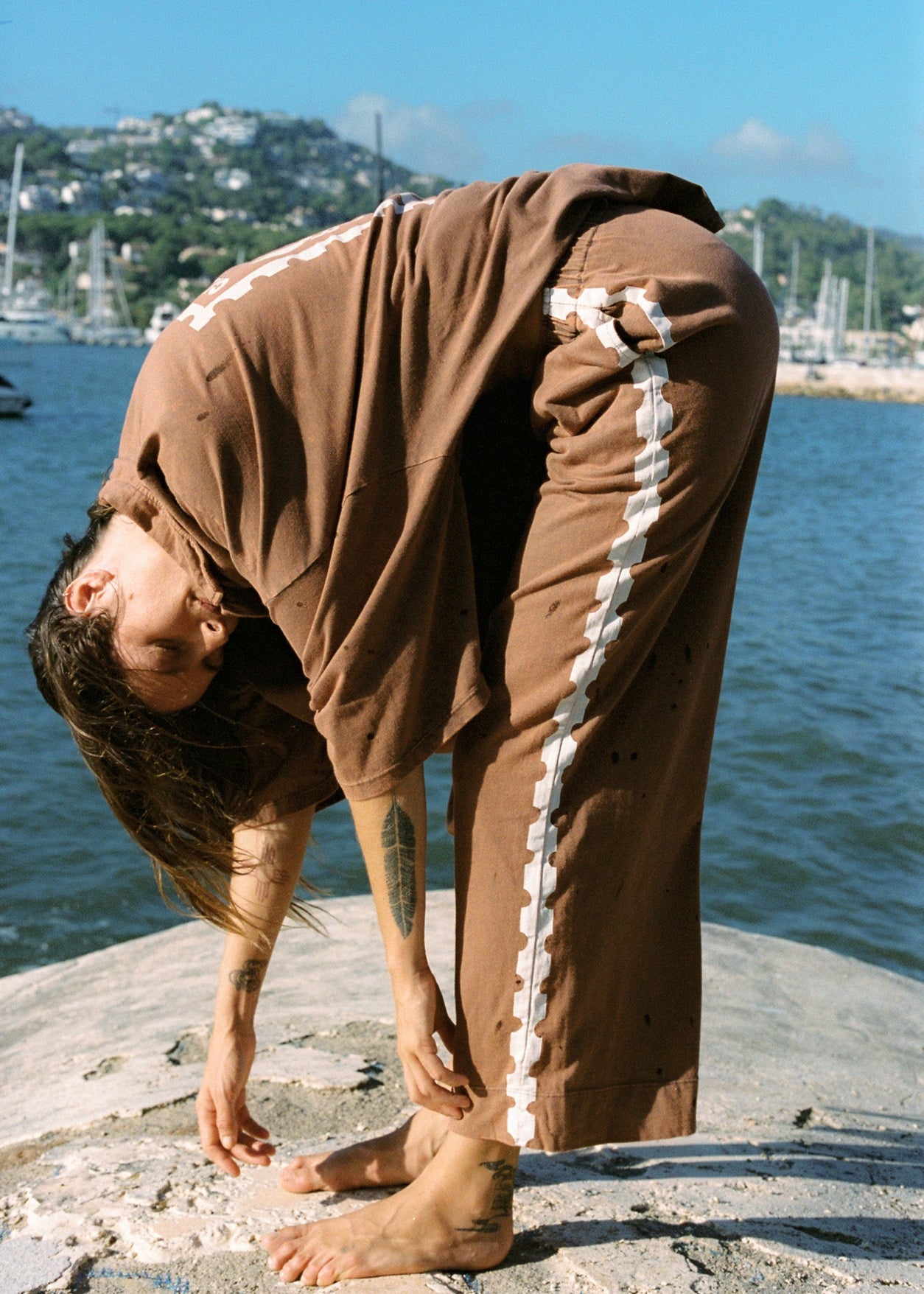 A person wearing brown bungalow pants with white side detailing and a matching oversized button up top