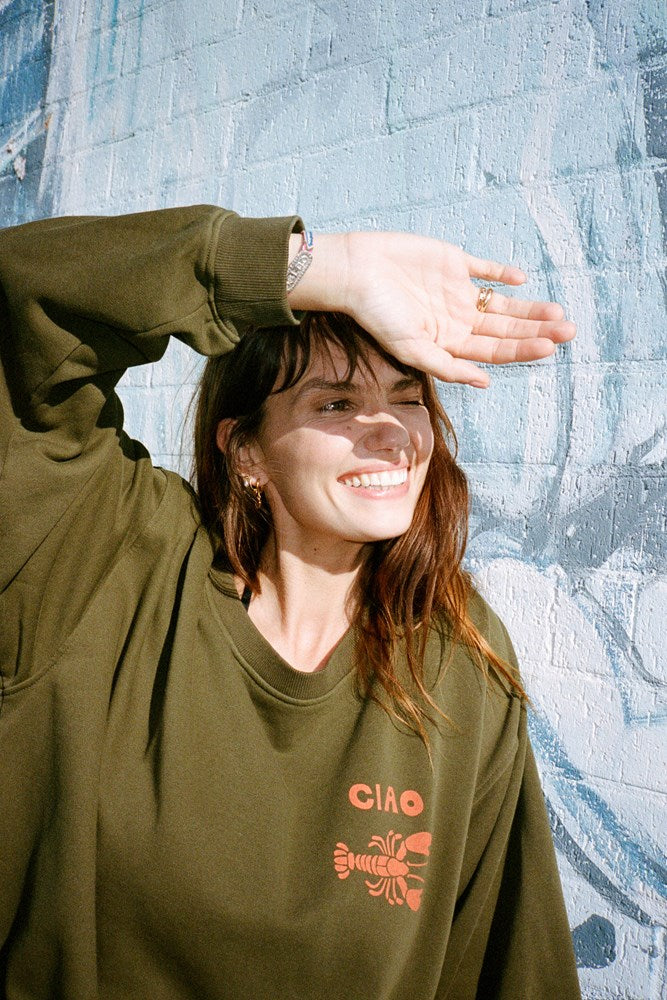 Person wearing a green jumper with an orange lobster graphic design and ciao writing 