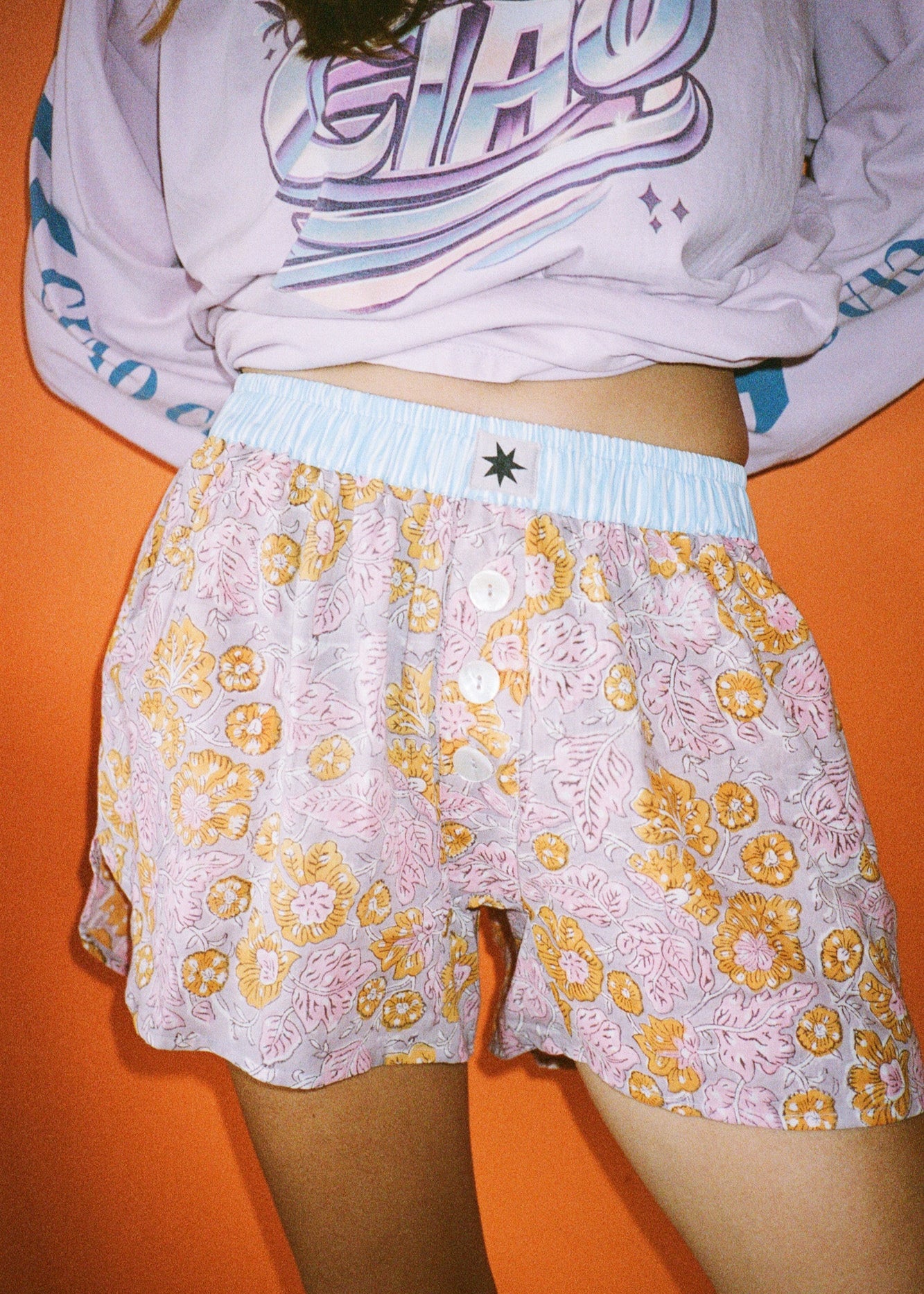 Person wearing pink and orange botanical printed boxer shorts with blue elasticated waist band