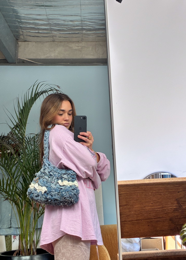 Woman taking a mirror selfie holding a unique up-cycled denim knot shoulder bag by the water