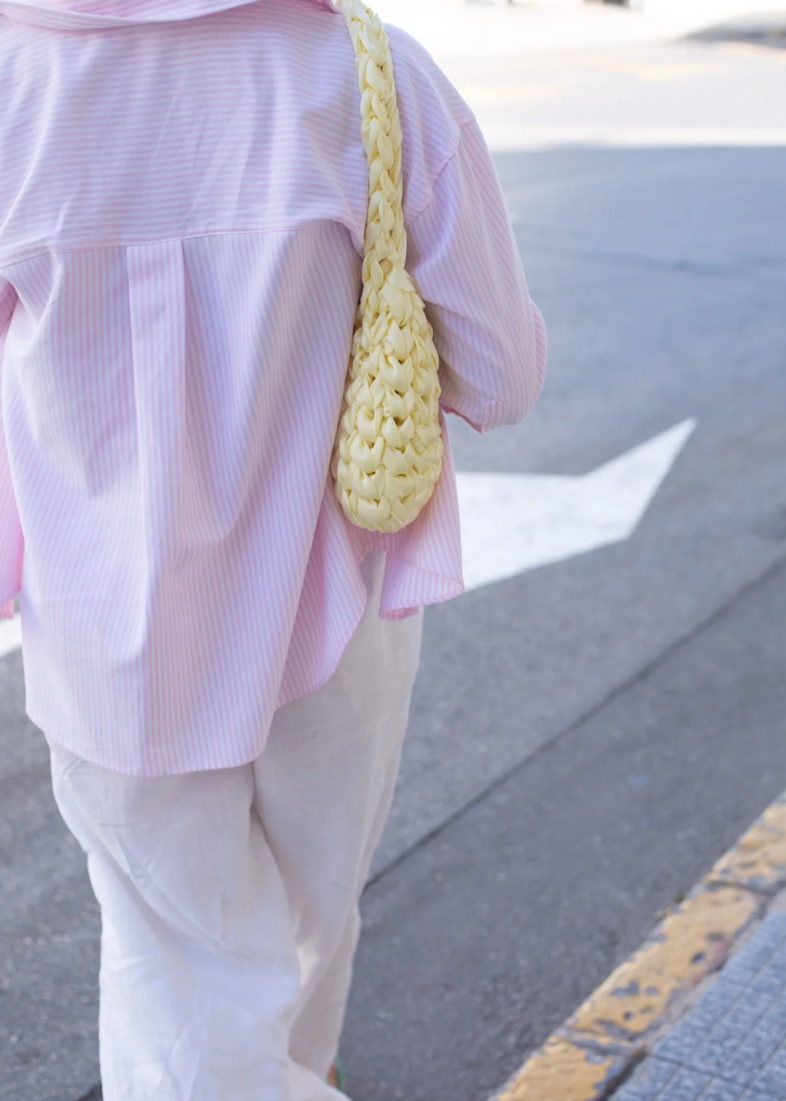 Person wearing a light yellow satin knot woven shoulder bag