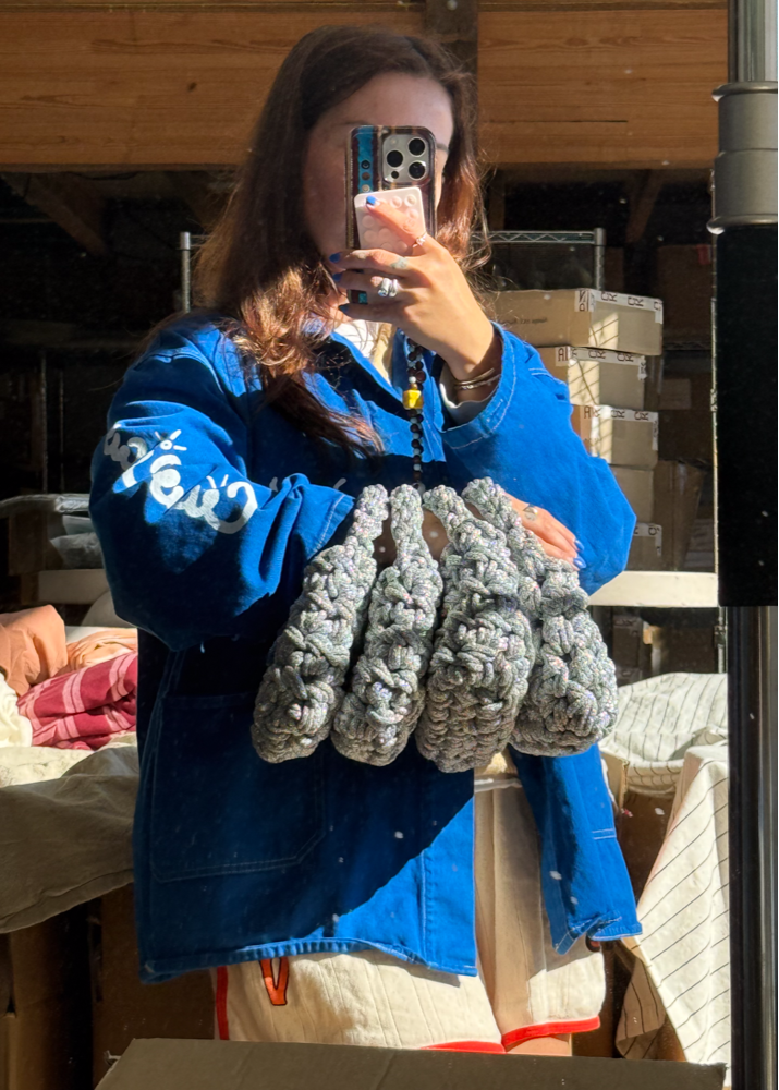 Woman taking a mirror selfie with grey, sparkly, metallic knot knitted handbags
