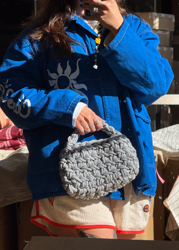 Person holding a grey, sparkly, metallic knot knitted handbag  