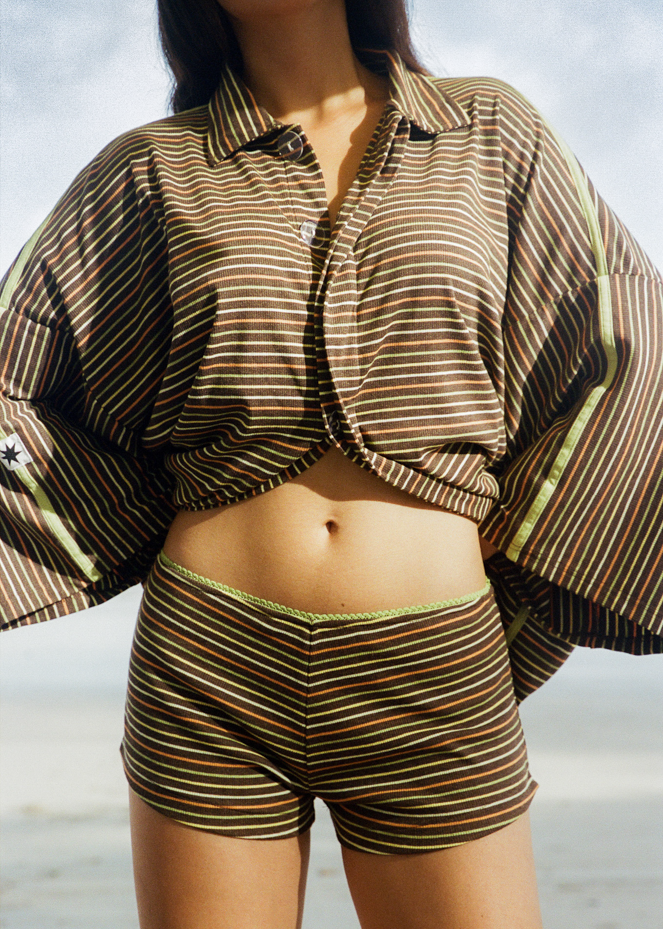 Woman in brown oversized shirt and mini short coordinated set with orange, yellow and green stripes 