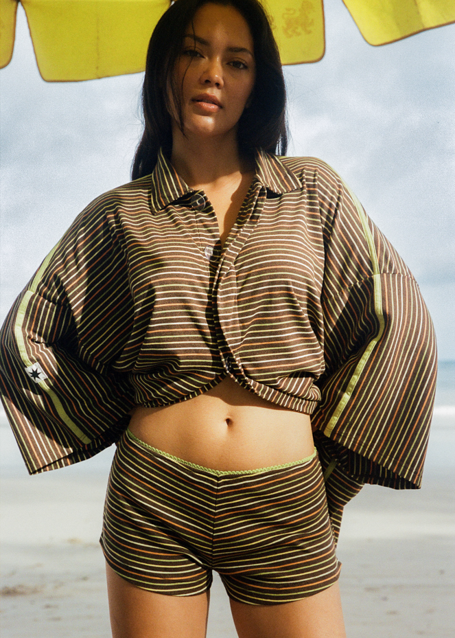 Woman in brown oversized shirt and mini short coordinated set with orange, yellow and green stripes 