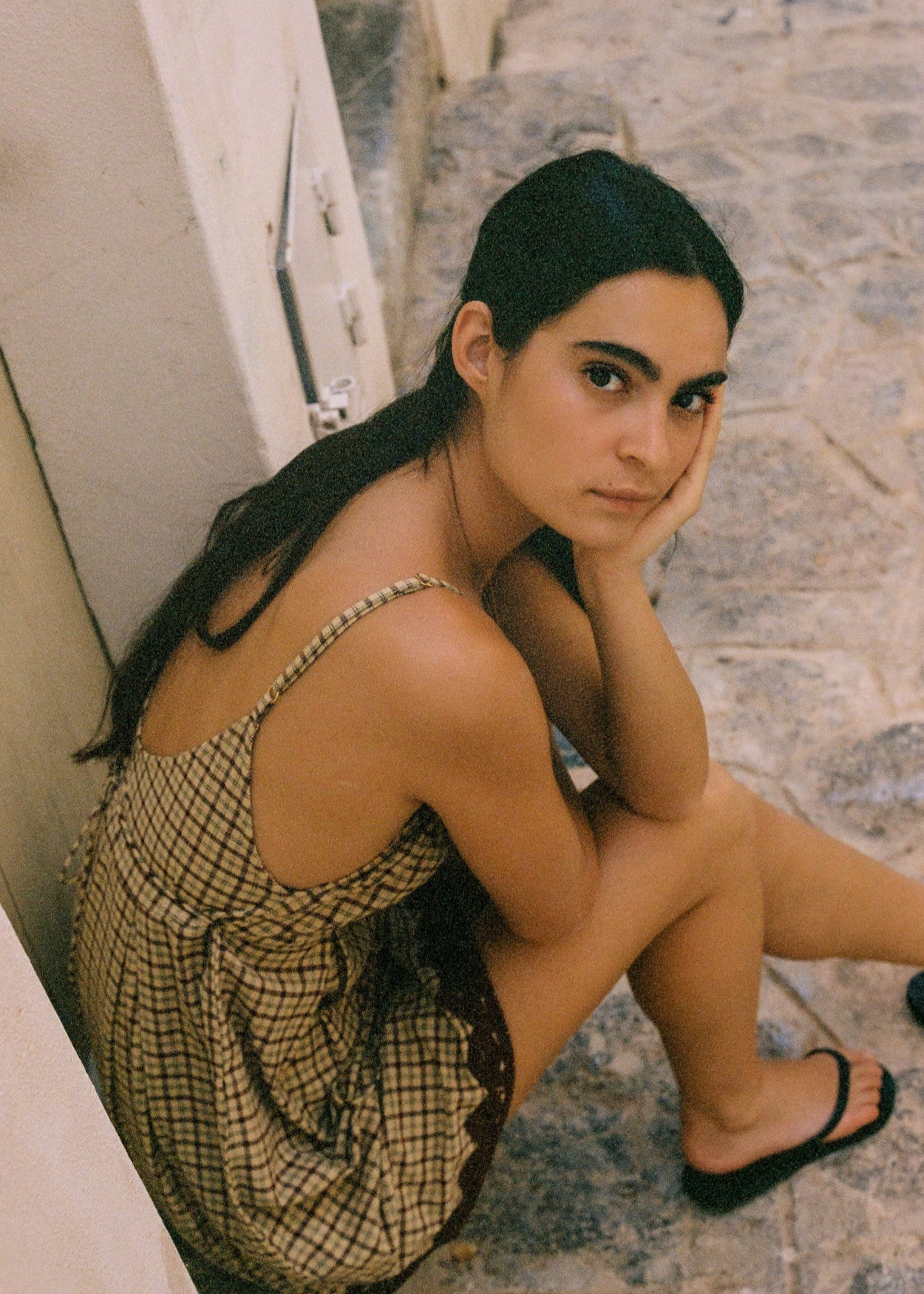 Woman sitting on a stone staircase wearing a checkered baby doll dress.