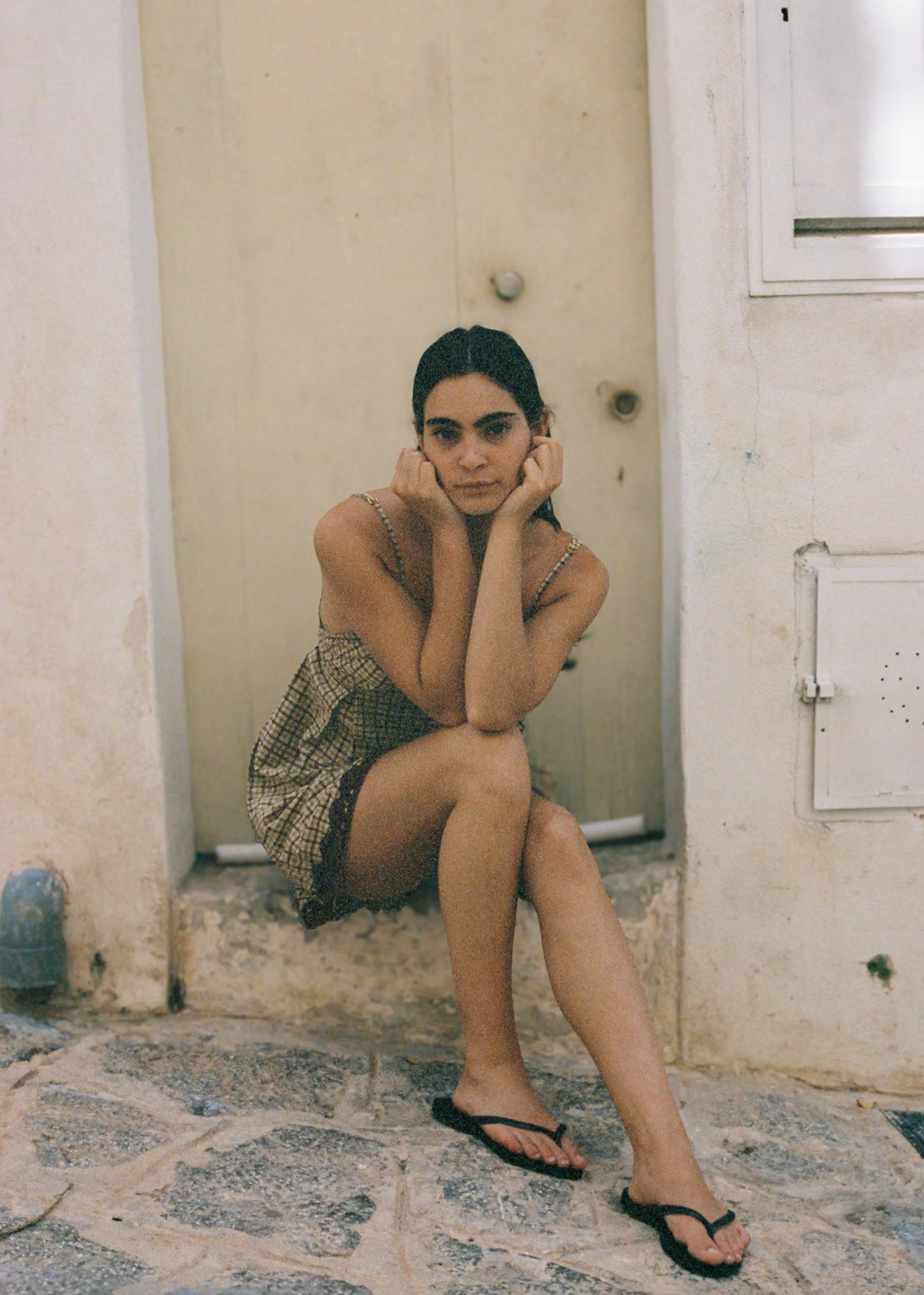 Woman sitting on a stone floor in a narrow alleyway wearing a babydoll dress.