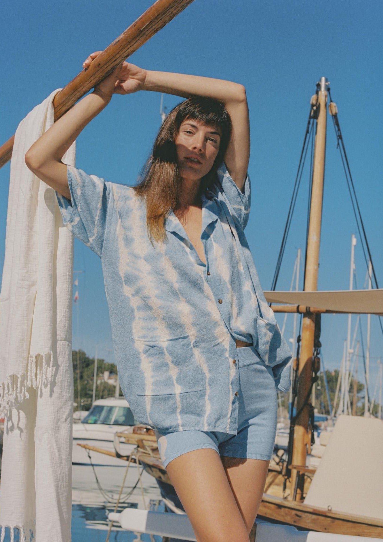 A person standing by a sailboat wearing a short-sleeved, button-up, tie-dye shirt in shades of blue and white.
