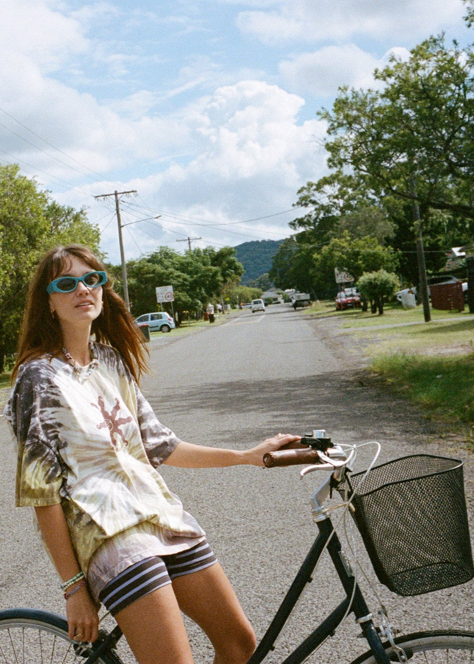 Woman riding a bicycle on a sunny day with a purple and green tie-dye box tee.